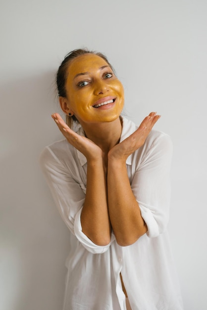 La donna mette una maschera d'oro sul viso sorridente Casa bagno luminoso Cura della pelle naturale