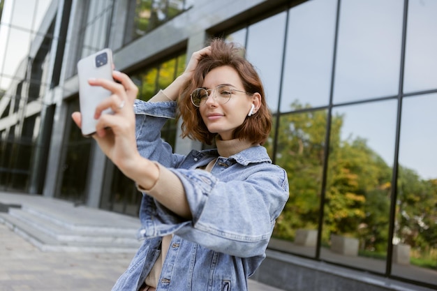La donna moderna ed elegante in abiti casual fa selfie sullo smartphone all'aperto in città