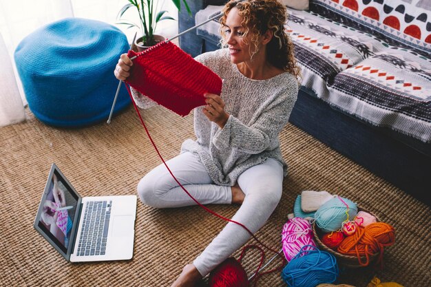 La donna moderna lavora a maglia a casa grazie ai contenuti video tutorial online sul computer portatile e alla connessione wireless. Concetto di nuova opportunità di lavoro e creatore di contenuti