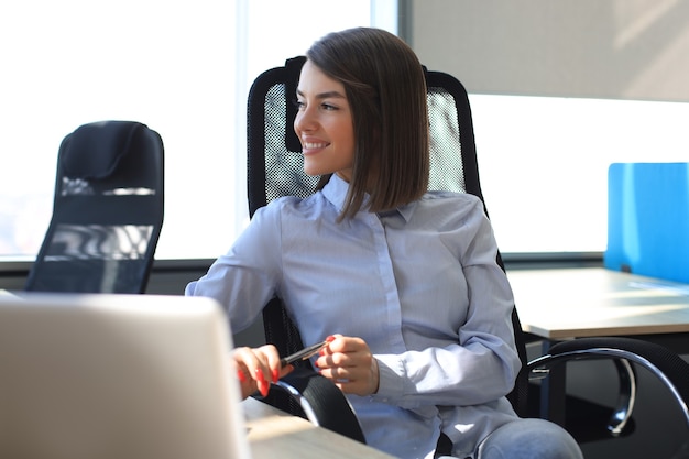 La donna moderna sorridente sta pensando agli affari mentre lavora in ufficio.