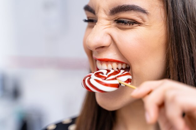 La donna morde la lecca-lecca con i denti sani bianchi. Bella signora con caramelle.