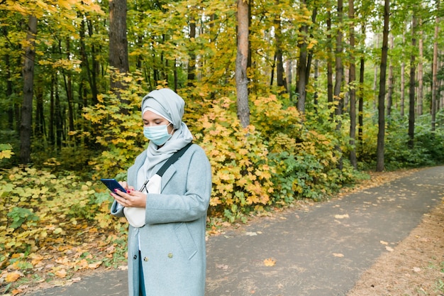 La donna musulmana con l'hijab indossa la maschera facciale all'aperto. Coronavirus, assistenza sanitaria e concetto di pandemia. Copia spazio