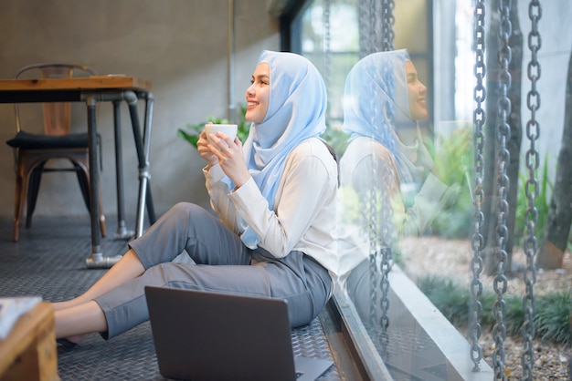 La donna musulmana con l'hijab sta lavorando con il computer portatile in caffetteria