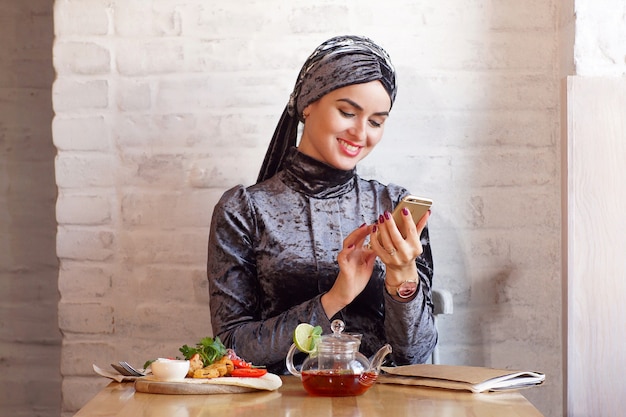 La donna musulmana conduce la corrispondenza al telefono seduto in un caffè