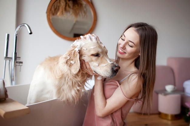 La donna nel bagno lava il cane e applica lo shampoo per la lana La ragazza bagna il golden retriever