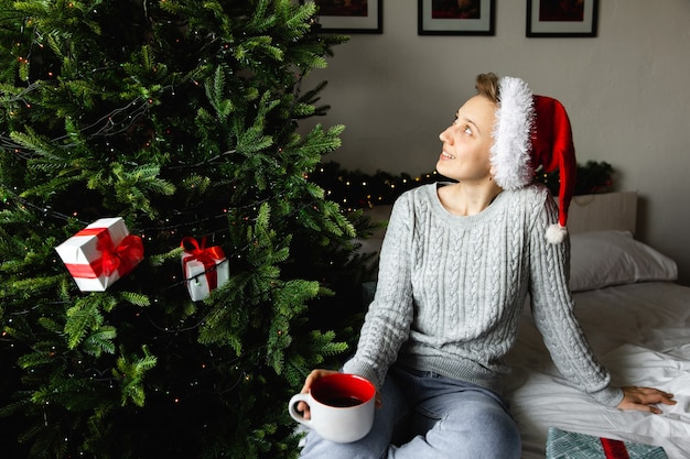 La donna nel sorriso rosso del cappello della Santa guardando un albero di Natale