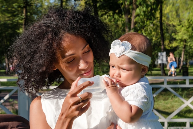 La donna nera dà l'acqua al suo bambino usando il biberon nel parco estivo.