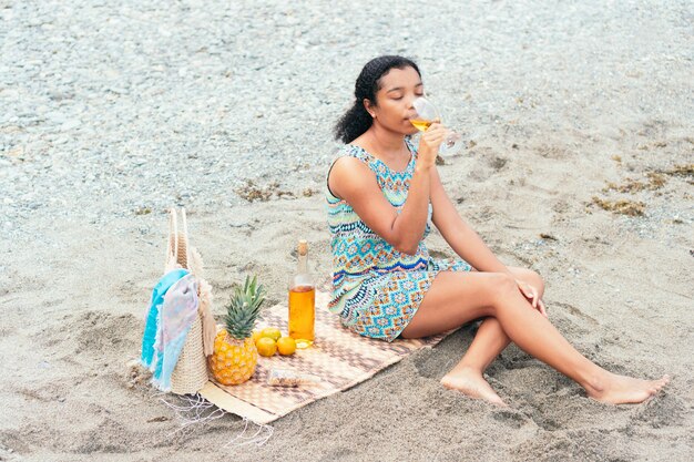 La donna nera si gode un bicchiere di vino sulla spiaggia al mattino