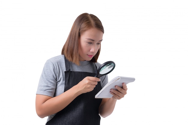 La donna o il meccanico del lavoratore in camicia e grembiule grigi sta tenendo il blocco note e usano la lente d&#39;ingrandimento isolata