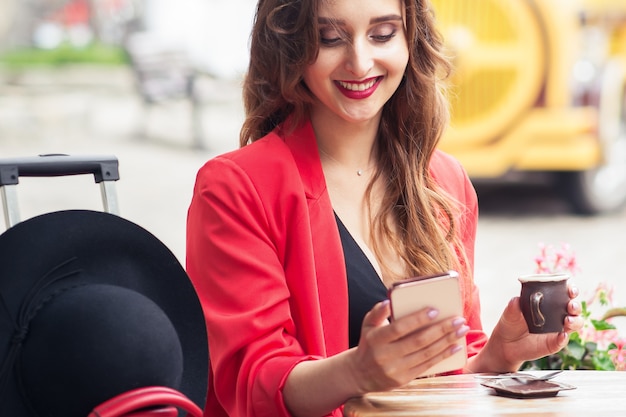 La donna osserva nello smartphone che si siede al caffè all'aperto.