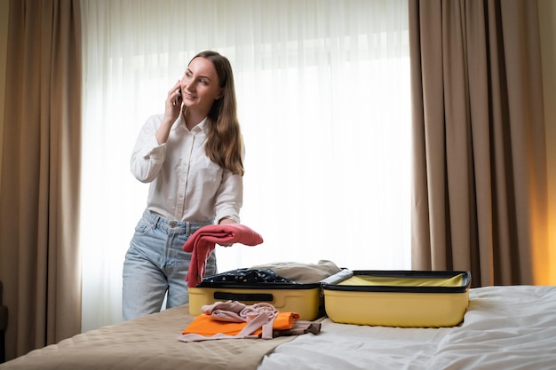 La donna parla al telefono mentre prende i vestiti dalla valigia