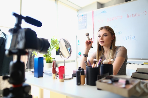 La donna parla di cosmetici con palette di fard di ombretti e pennelli che registrano video online