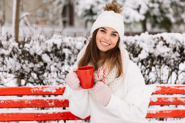 La donna passa in guanti che tengono una tazza accogliente con cioccolata calda, tè o caffè e un bastoncino di zucchero.