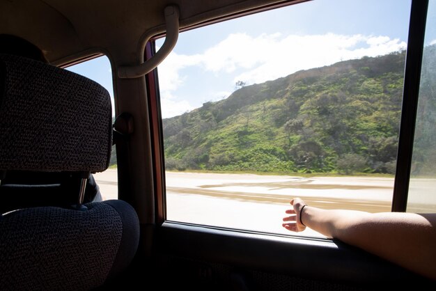 La donna passa la finestra godendosi la brezza mentre si guida in auto in riva al mare in un giorno d'estate