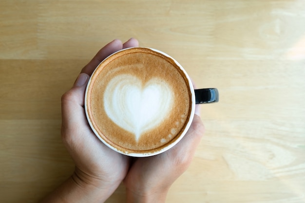 la donna passa la tazza di caffè della tenuta con arte del latte di mattina con luce solare sulla tavola