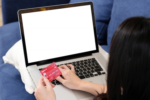 La donna passa la tenuta della carta di credito e il computer portatile di battitura a macchina con lo schermo in bianco. concetto di pagamento bancario internet