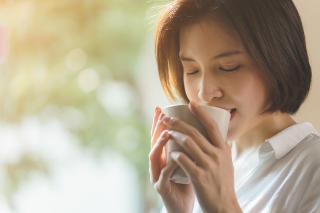 La donna passa la tenuta della tazza di caffè o del tè calda alla luce solare di mattina.