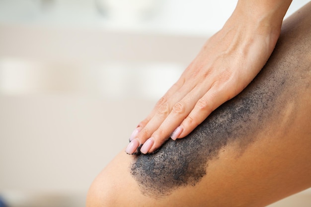 La donna per la cura della pelle applica uno scrub nero con sale marino