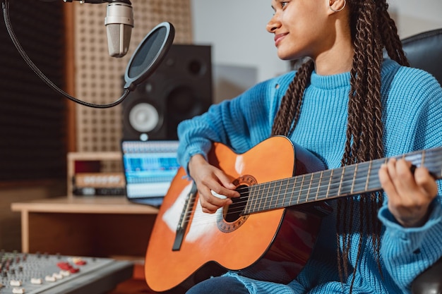 La donna piacevole del primo piano con il musicista di dreadlocks alla moda suona la chitarra e registra una nuova canzone