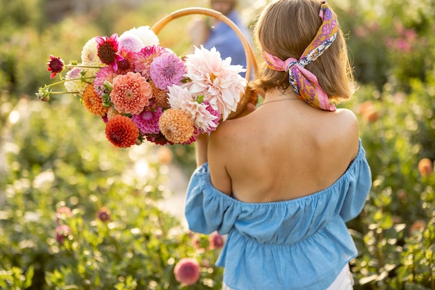 La donna porta sulla spalla tanti fiori colorati nella fattoria delle dalie