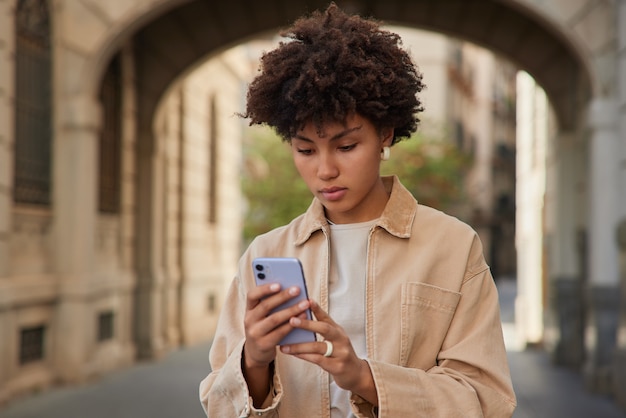 la donna posa in un ambiente urbano con lo smartphone digitale naviga in internet indossa una giacca beige sta fuori ha una vacanza di viaggio da sola