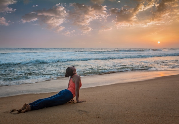 La donna pratica yoga asana Urdhva Mukha Svanasana in spiaggia