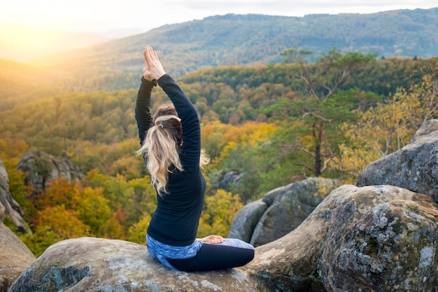 La donna pratica yoga e fa asana sulla cima dell&#39;enorme macigno di sera