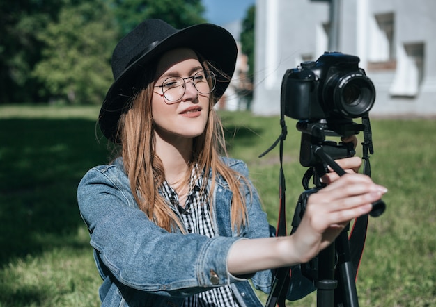 La donna prende la foto con la macchina fotografica professionale sul treppiede nel parco dell&#39;estate