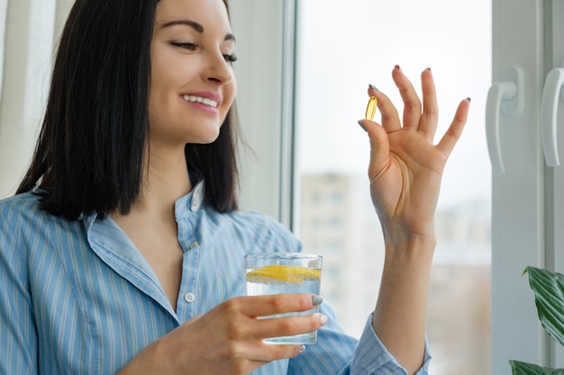 La donna prende la pillola con omega-3 e tiene un bicchiere di acqua fresca con limone
