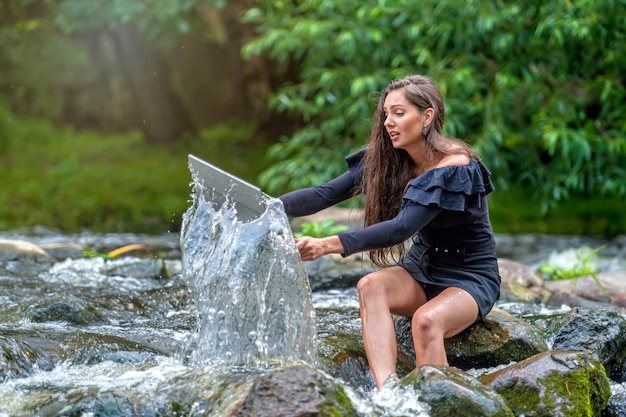 La donna preoccupata tira fuori dall'acqua il laptop caduto in un incidente di lavoro durante le vacanze a distanza sul fiume