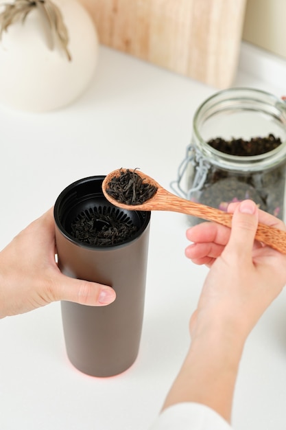 La donna prepara il tè in una tazza termica marrone da portare con sé mentre tiene in mano un simpatico cucchiaio di legno