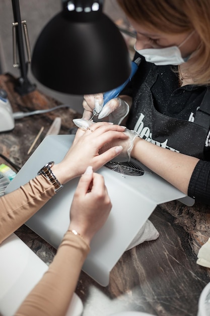 La donna professionista in maschera medica protettiva fa la manicure in uno studio di bellezza express Concetto di cura delle mani e delle unghie