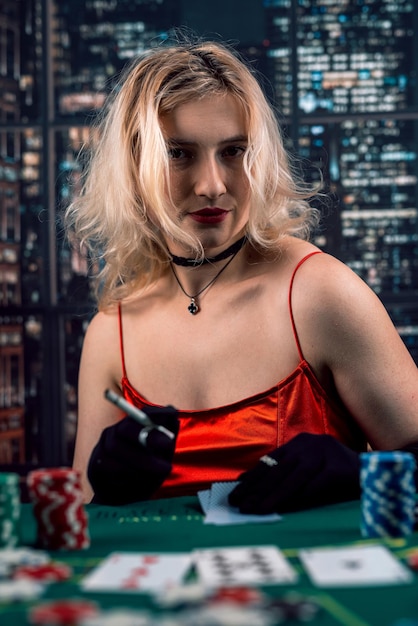 La donna ricca indossa un abito rosso da sera che gioca a poker tenendo il sigaro Gioco di poker