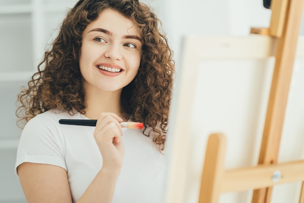 La donna riccia con un pennello artistico che dipinge un quadro sul cavalletto