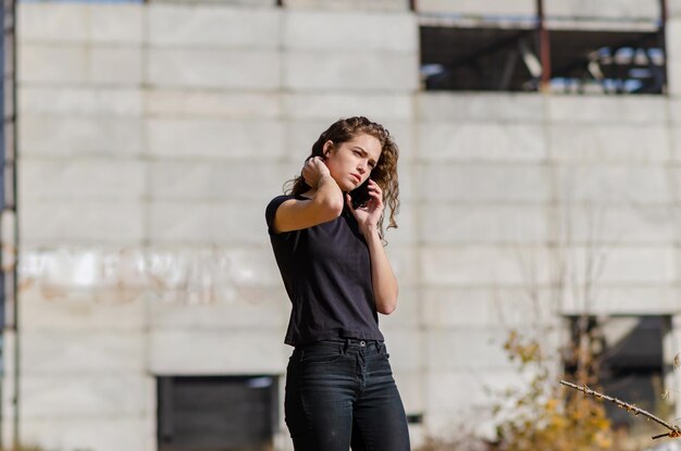 La donna riccia sexy sta parlando su un telefono cellulare Maglietta nera e jeans Sfondo sfocato