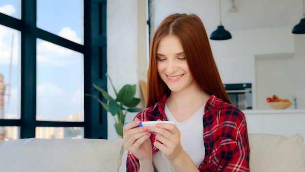 La donna rossa della ragazza caucasica incinta della futura madre felice guarda il risultato positivo del test di gravidanza