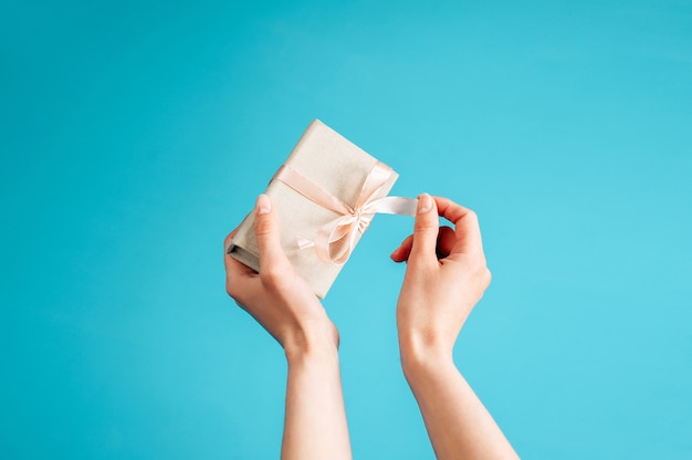 La donna scompatta un regalo. Mani della donna con la presente casella su sfondo blu.