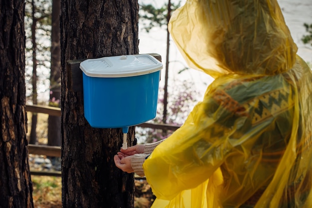La donna sconosciuta in impermeabile giallo si lava le mani nel lavabo appeso all'albero. Mattinata piovosa in campo turistico nella foresta vicino al fiume.
