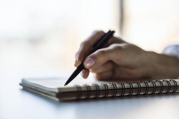 La donna scrive con una penna nel diario in un ufficio soleggiato concetto di affari e istruzione Primo piano