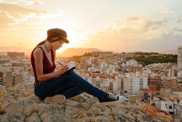 La donna scrive nel suo taccuino frasi e pensieri all'aperto al tramonto