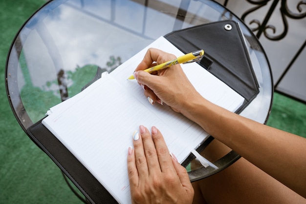 La donna scrive su un quaderno con una penna mentre è seduta al tavolo di casa sul terrazzo