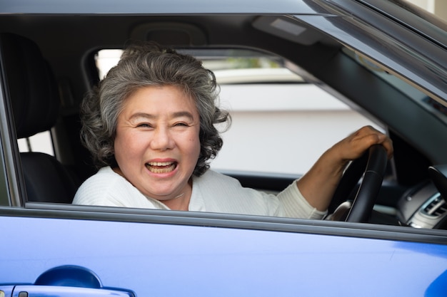 La donna senior asiatica che guida un'automobile e sorride felicemente con l'espressione positiva felice durante l'azionamento per viaggiare viaggio, la gente gode ridere del trasporto e guida attraverso il concetto