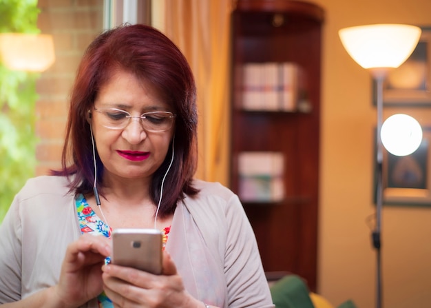 La donna senior che usando la nuova tecnologia chiama con il suoi smpartphone e cuffie