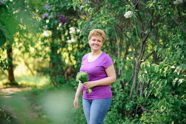 La donna senior in maglietta e jeans tiene un mazzo di fiori.