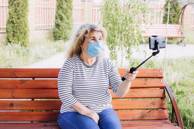 La donna senior indossa la maschera protettiva contro le malattie infettive e l'influenza e la fabbricazione di selfie, concetto di sanità. quarantena per il coronavirus.