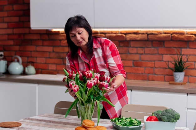 La donna senior mette i fiori in ordine prima di cena in cucina