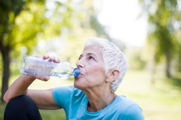 La donna senior riposa e beve l'acqua dopo l'allenamento