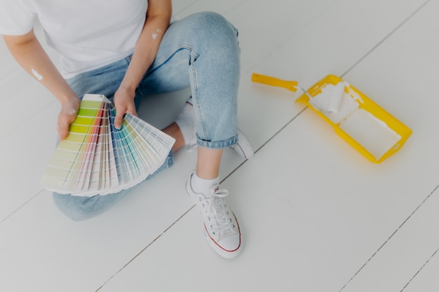 La donna senza volto in jeans detiene campioni di colore, sceglie il tono migliore per i muri di ristrutturazione