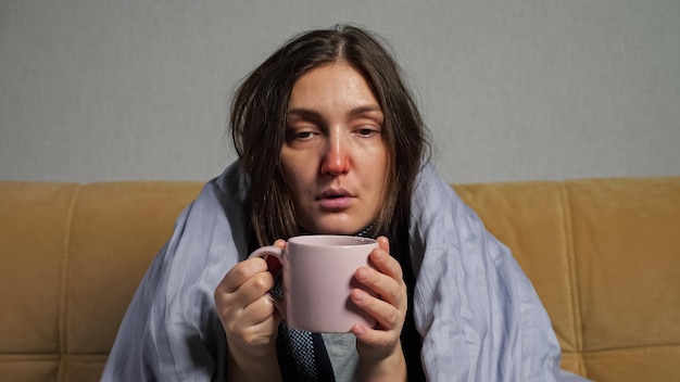 La donna si ammala e beve il tè avvolta in una coperta sul divano