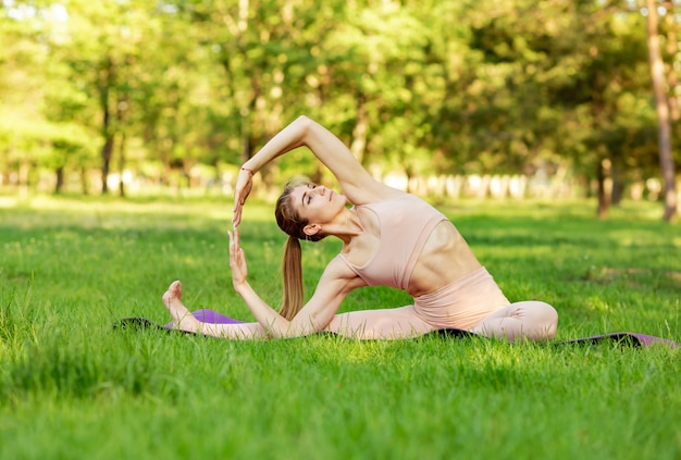 La donna si esercita in yoga su una priorità bassa degli alberi e dell'erba verdi